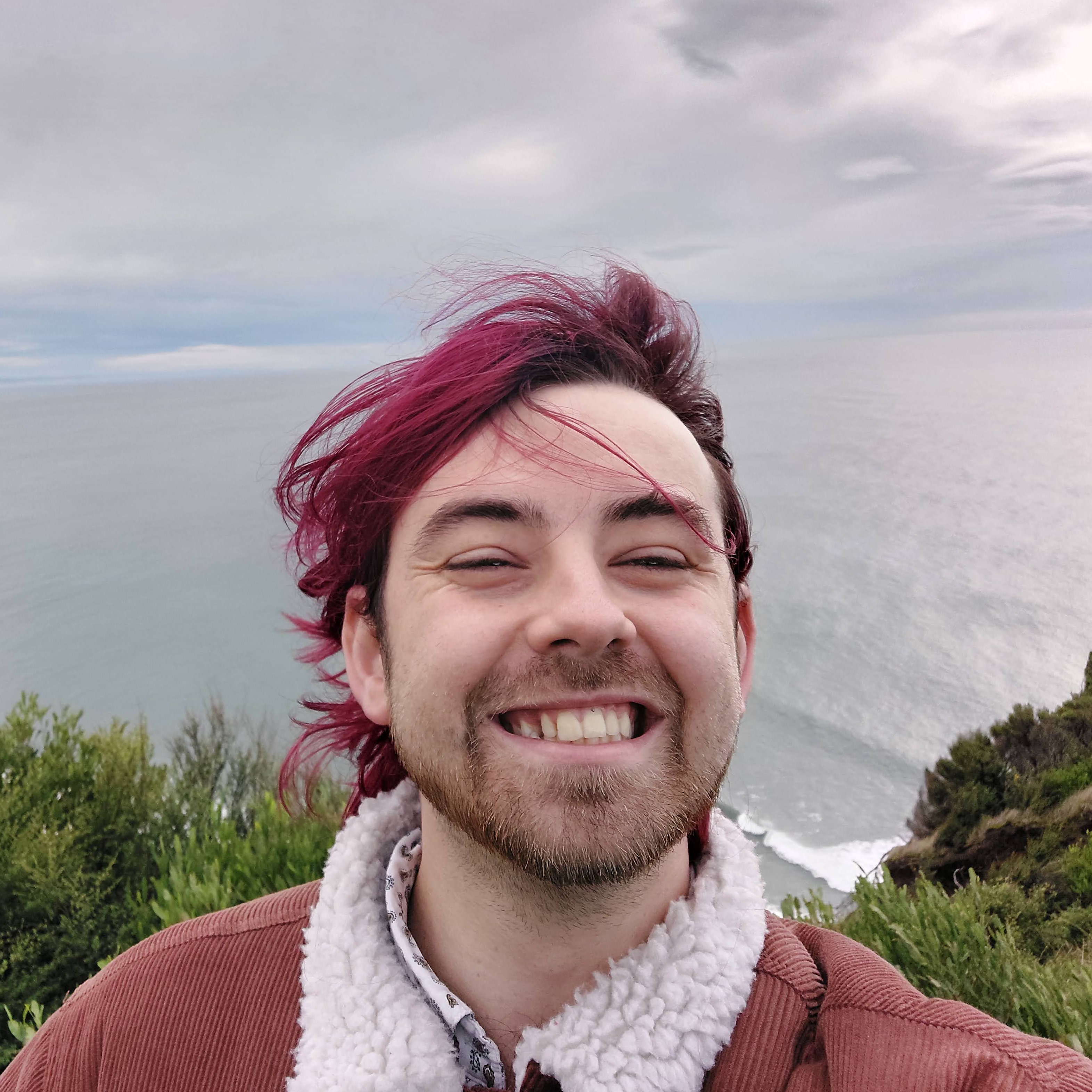 Photo of Java smiling upon a clifftop in Raglan, NZ.